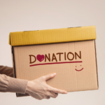 Se ve el torso y los brazos de una persona ofreciendo una caja cn el texto DONATION